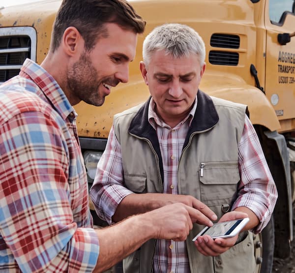 Two men in front of heavy machinery reviewing something on a smartphone
