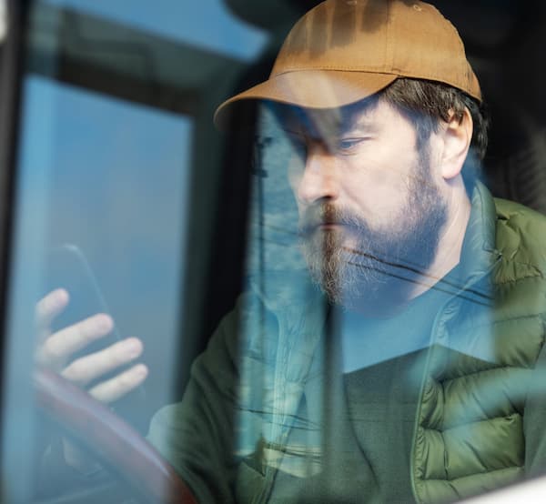 Truck driver in a parked truck sitting in the driver's seat looking at his phone