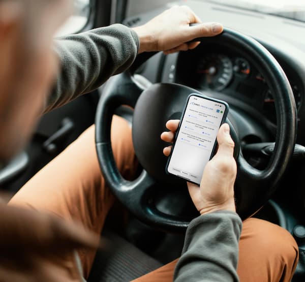 Shot of a truck driver sitting in the driver's seat, holding out their phone in front of the steering wheel